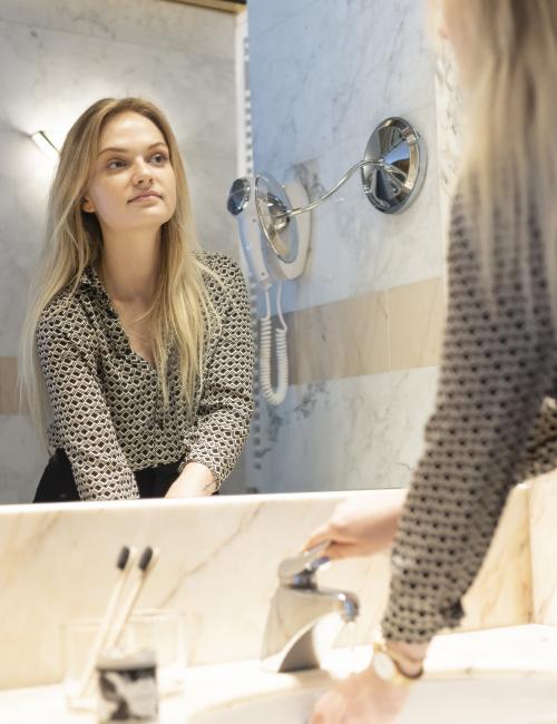 Junge Frau im Badezimmer aus Marmor, schaut beim Händewaschen in den Spiegel