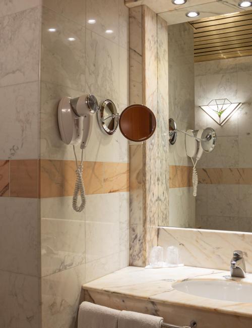 Blick ins Marmor-Badezimmer mit großem Waschtisch, Wandspiegel, Schminkspiegel und Fön
